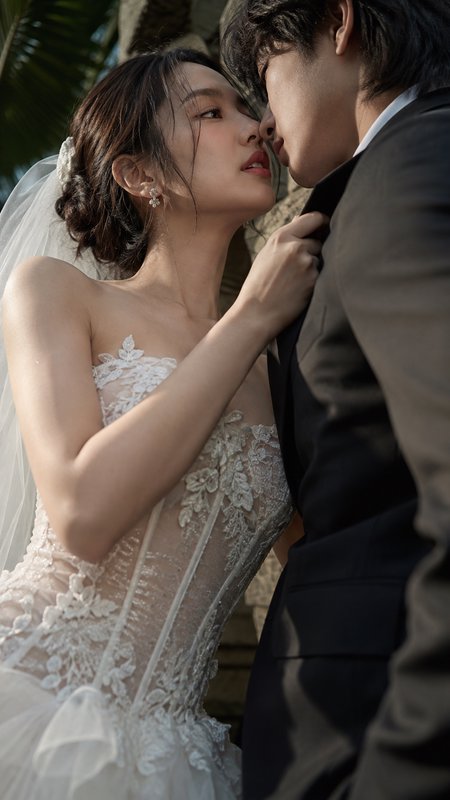Intimate close-up of bride in lace wedding dress leaning in to kiss her groom during an outdoor tropical wedding photoshoot