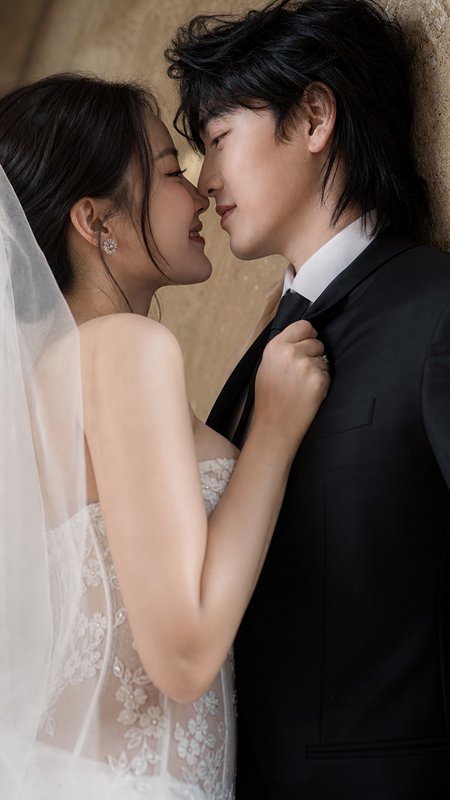 Intimate wedding portrait of a bride tugging her groom's tie as they lean in close to share a tender near-kiss.