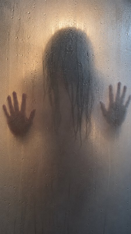 Long-haired silhouetted figure pressing both hands against fogged condensation-covered shower glass