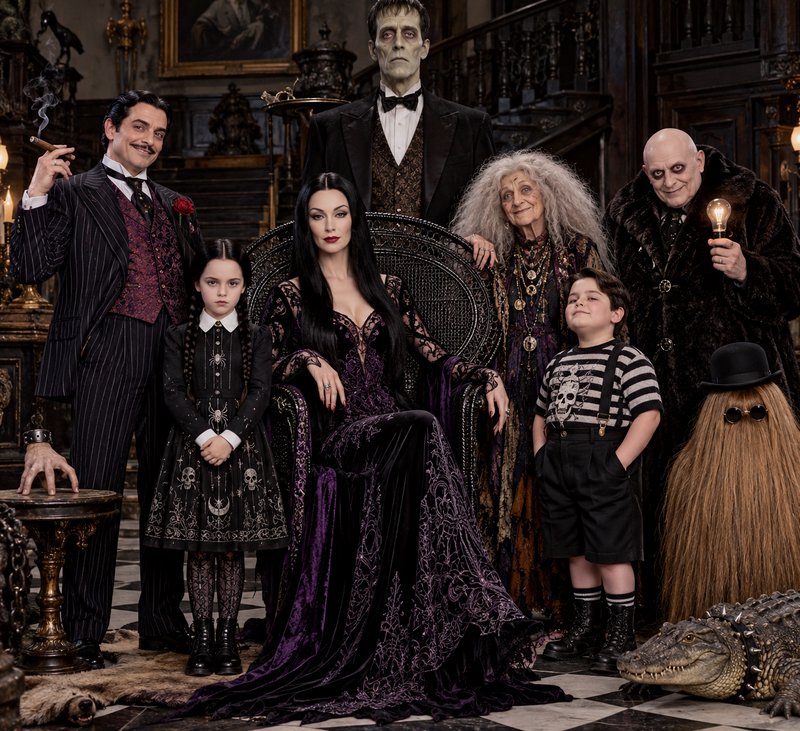 Full Addams Family cast posed for a formal group portrait inside their ornate gothic mansion