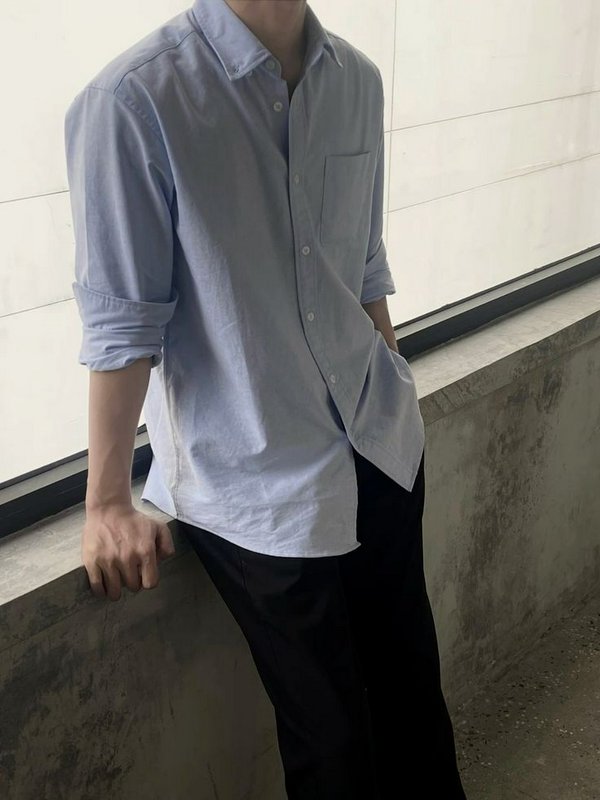Person wearing a light blue button-down shirt and black pants, leaning on a concrete railing.