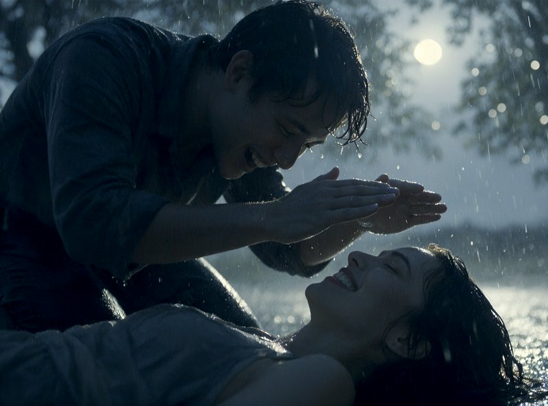 Joyful laughing young couple share a tender playful moment together outdoors in falling rain at t...