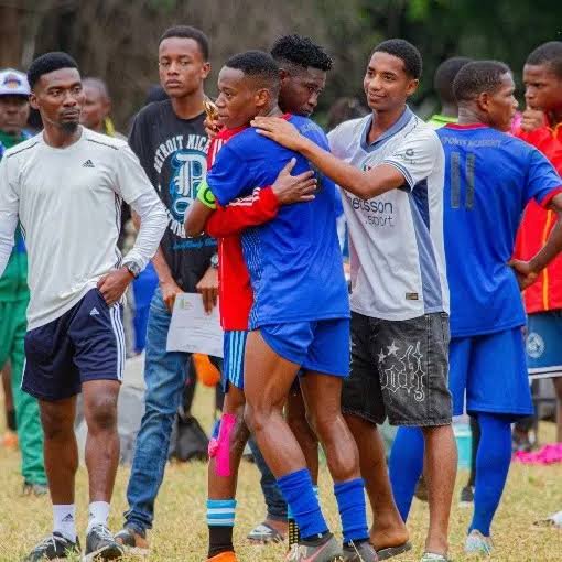 Group of soccer players hugging and celebrating on a grassy field.