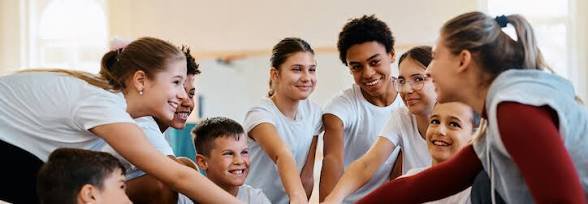 Diverse group of kids and teens in a circle, joining hands in a team-building activity.