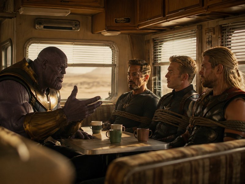 Thanos gestures as he speaks to rope-tied Iron Man, Captain America, and Thor seated at a dinette...