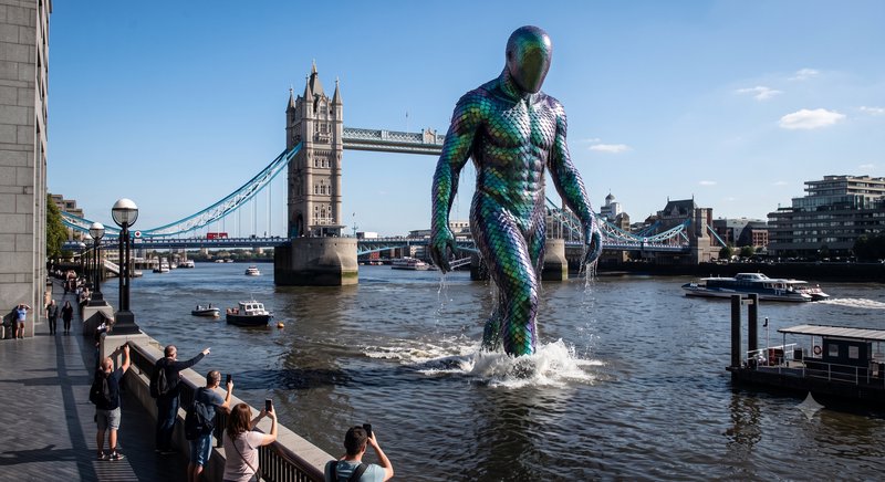 Giant iridescent scale-textured humanoid rises from the River Thames near Tower Bridge, London, a...