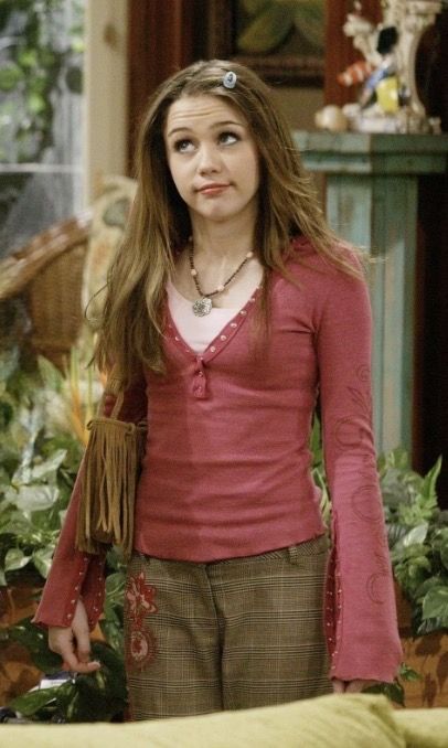 Young woman with long hair in a pink long-sleeve top and plaid pants indoors.
