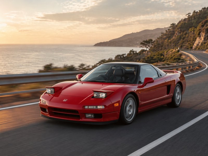 Red Honda NSX sports car driving along a coastal highway at sunset.