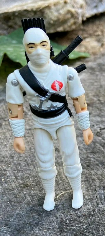 White-clad ninja action figure with swords and mask, standing outdoors.