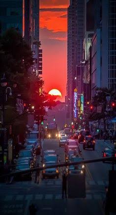 Fiery orange sunset framed between tall downtown skyscrapers over a busy evening city street with...