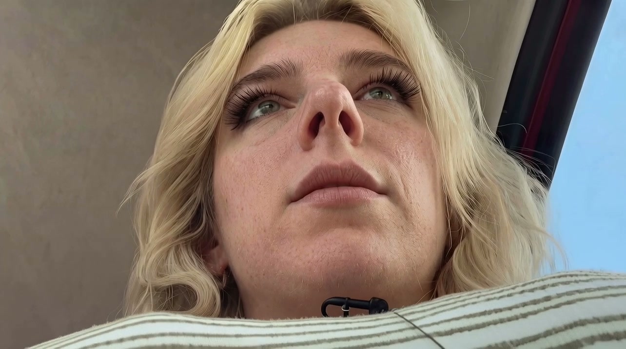 Close-up of a blonde woman looking upwards, seen from below with a small microphone near her neck.