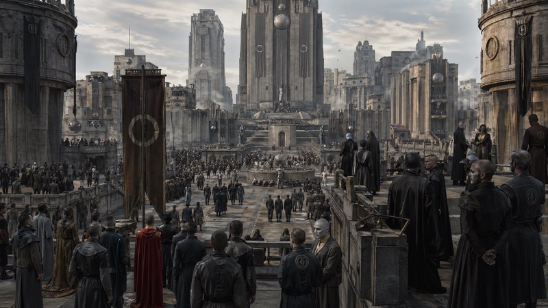 A grand futuristic/dystopian city square with stone towers and a large central statue, crowds gat...