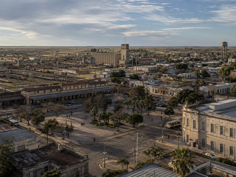 Aerial view of a historic town square with colonial buildings, palm trees, and a distant water to...