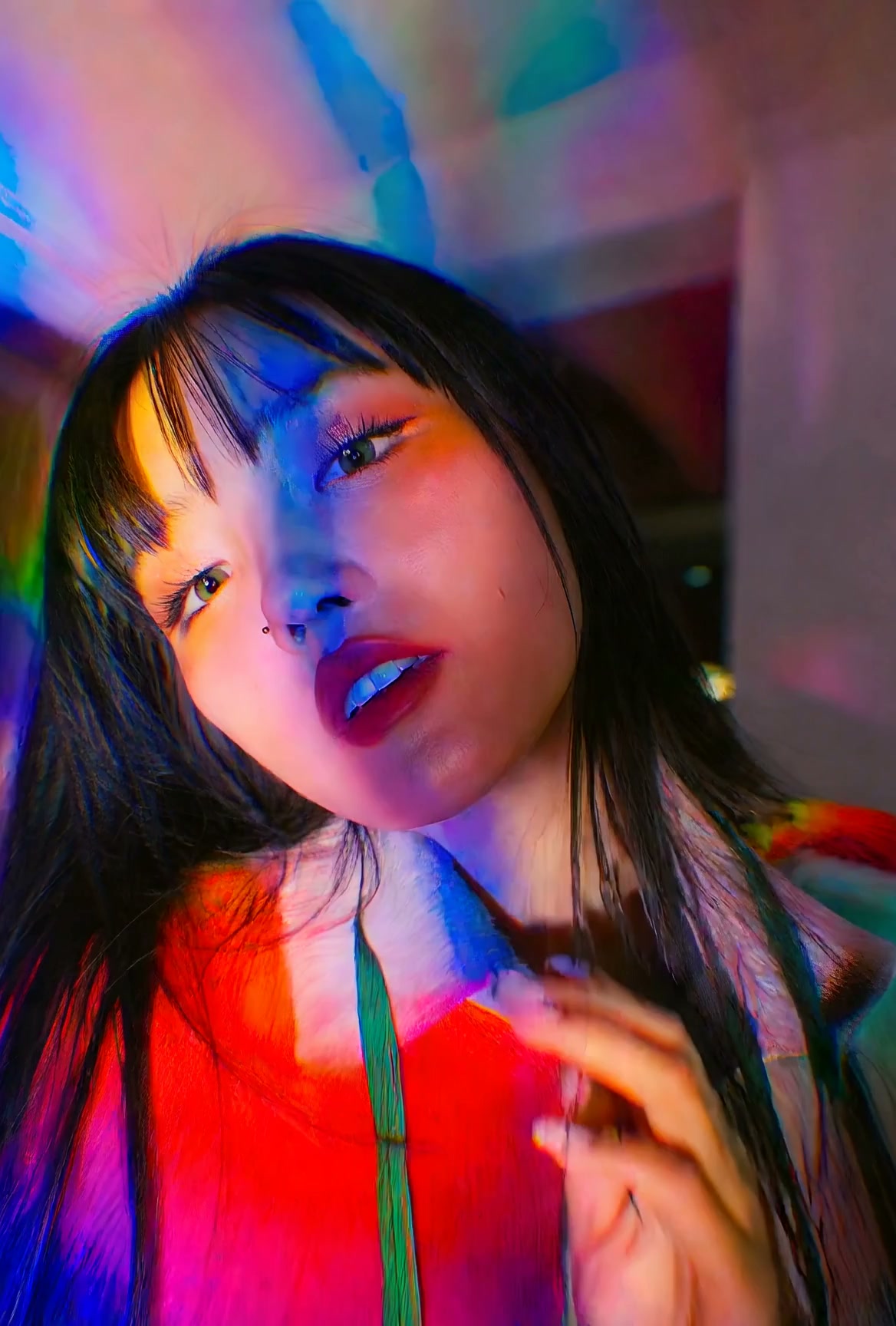 Young woman with straight black bangs lit by iridescent rainbow neon light in a closeup indoor po...