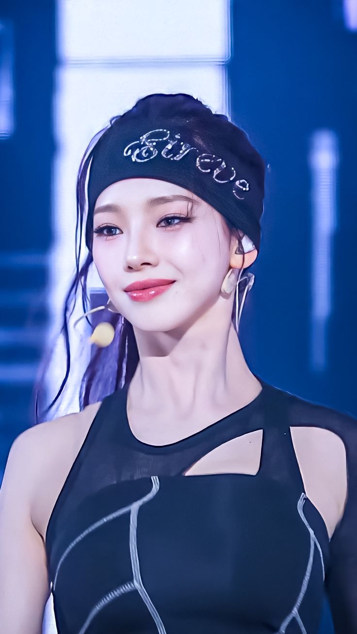 Close-up of a female performer on stage wearing a black headband and sleeveless outfit under blue lights.