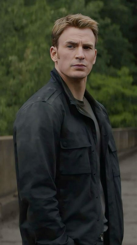 Portrait of a man in a dark jacket standing outdoors with green foliage in the background