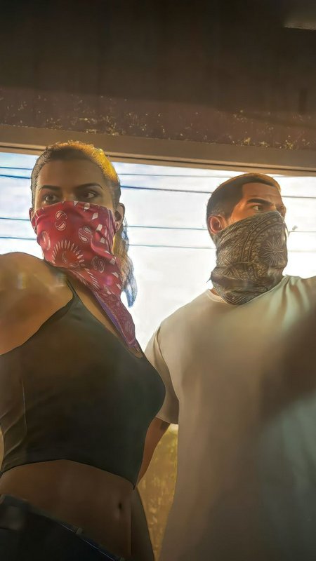 Low angle portrait of a couple standing together, both wearing paisley bandanas as face coverings near a sunlit window.