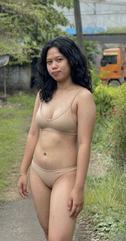 Woman in beige lingerie standing on a garden path outdoors.