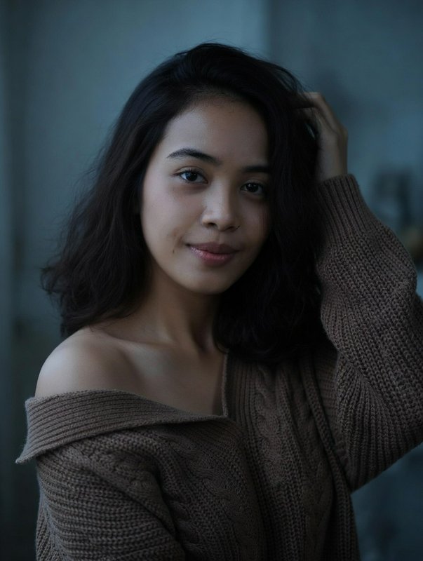 Portrait of a woman with dark hair in a chunky brown knit sweater under moody lighting