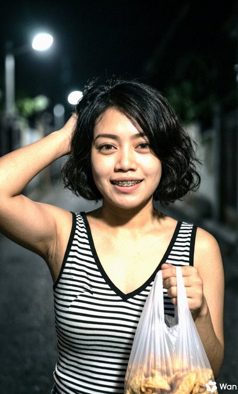 Young woman with braces in a striped tank top at night, holding a plastic bag of snacks.