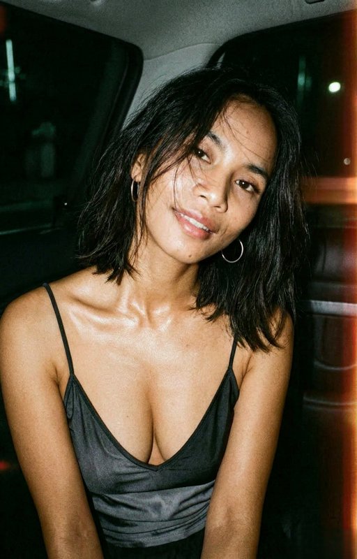 Portrait of a woman with short black hair wearing a black satin spaghetti-strap dress, smiling in...