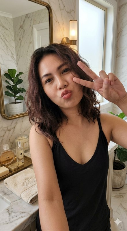 Young woman in a black tank top taking a selfie in a marble bathroom, flashing a peace sign