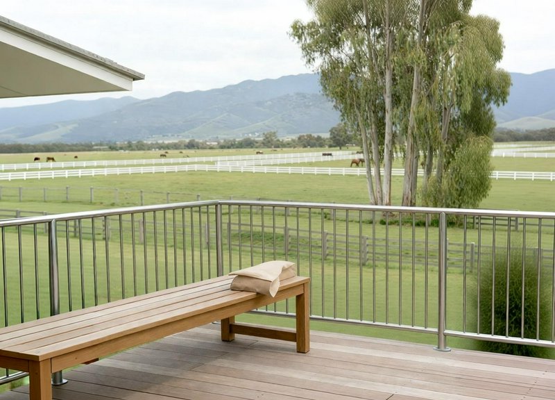 Wooden bench on a balcony overlooking a green pasture with trees and distant mountains.