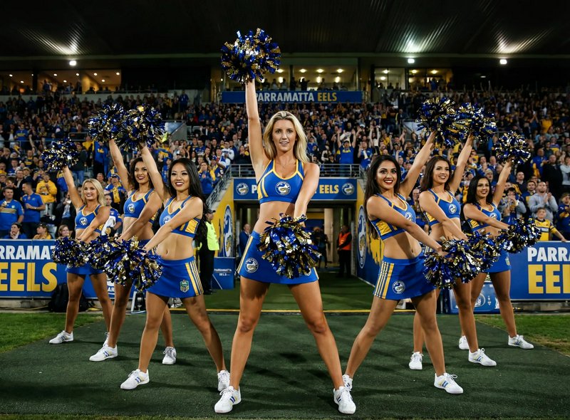 Cheerleaders in blue and yellow outfits performing with pom-poms on a stadium field.