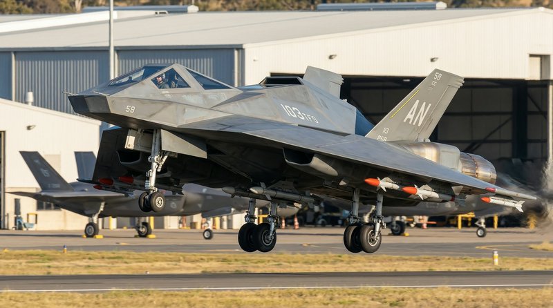 Stealth F-35 fighter jet lifting off the runway near a hangar, gray angular aircraft in flight.
