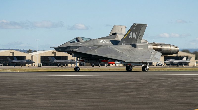 F-35 stealth fighter on taxiway at an airbase with gray angular fuselage and rear exhaust.