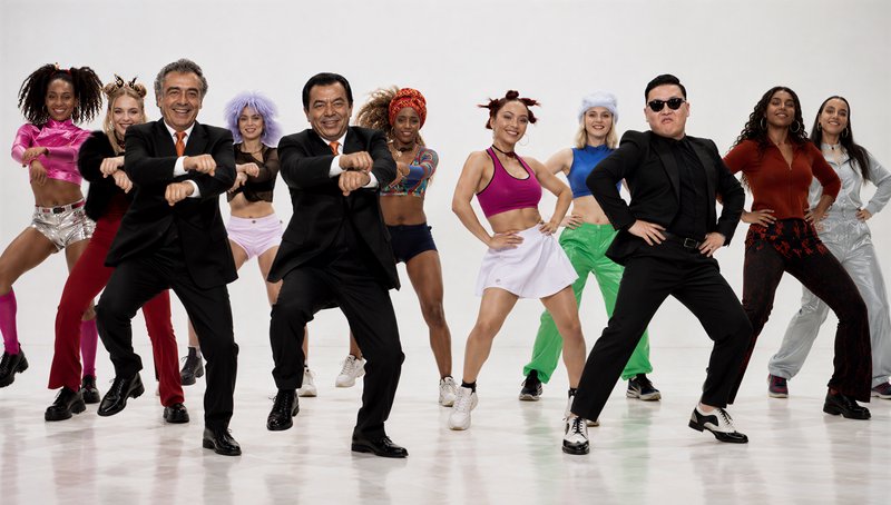 Diverse group of dancers strike synchronized Gangnam Style poses in a plain white studio