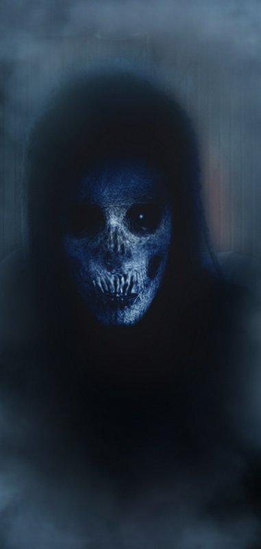 Hooded skeletal grim reaper apparition looms out of dark hazy blue fog