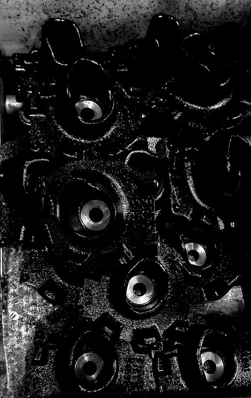 High contrast black and white close up of a grimy cast iron automotive engine cylinder head on a ...