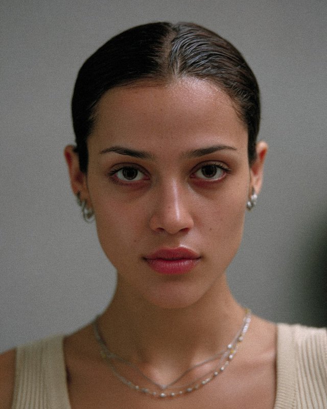 Close-up portrait of a young woman with slicked-back hair and neutral expression.