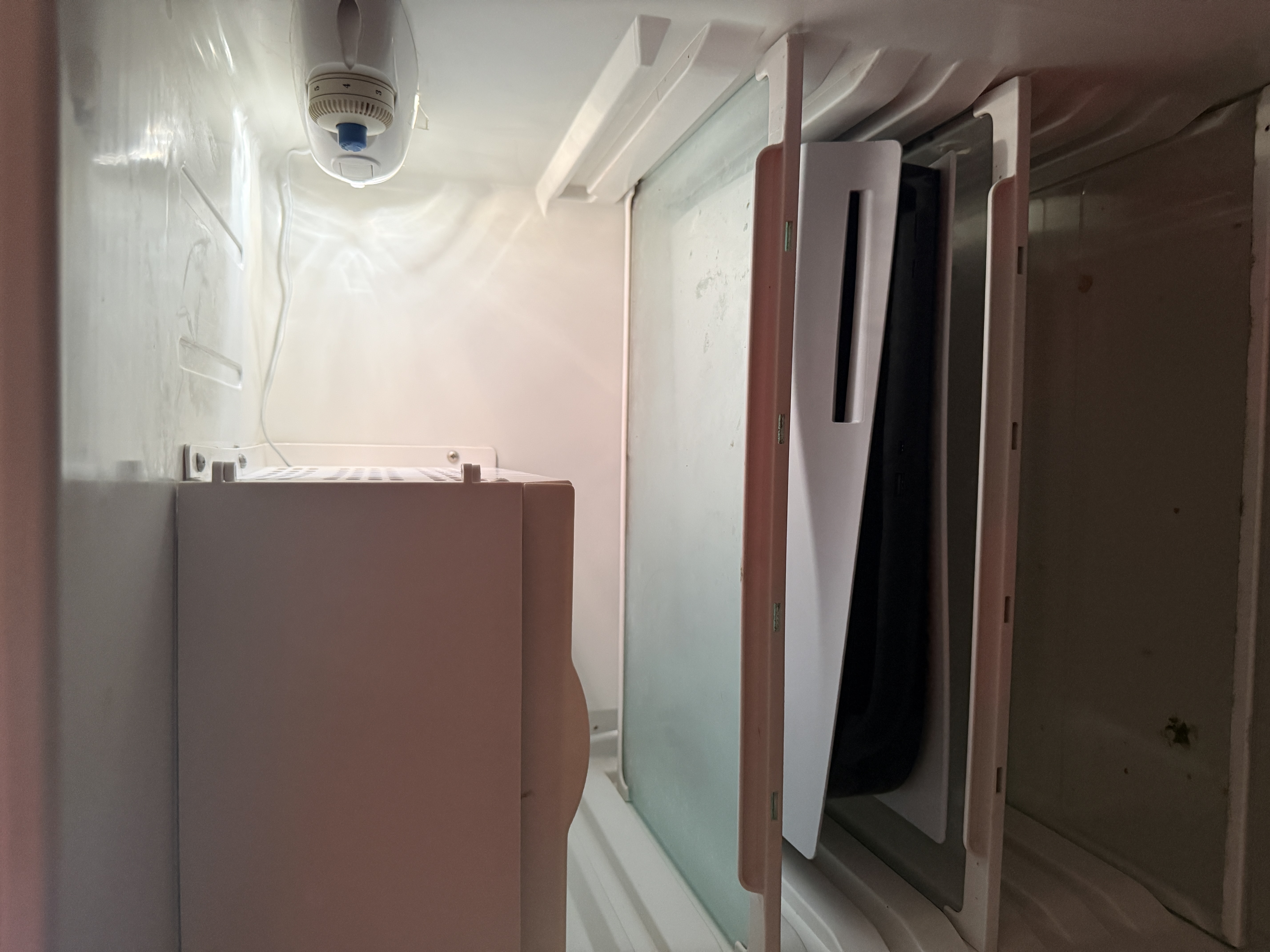 Small compact utility space with a security camera, white cabinet, and appliance panels in a narrow room.