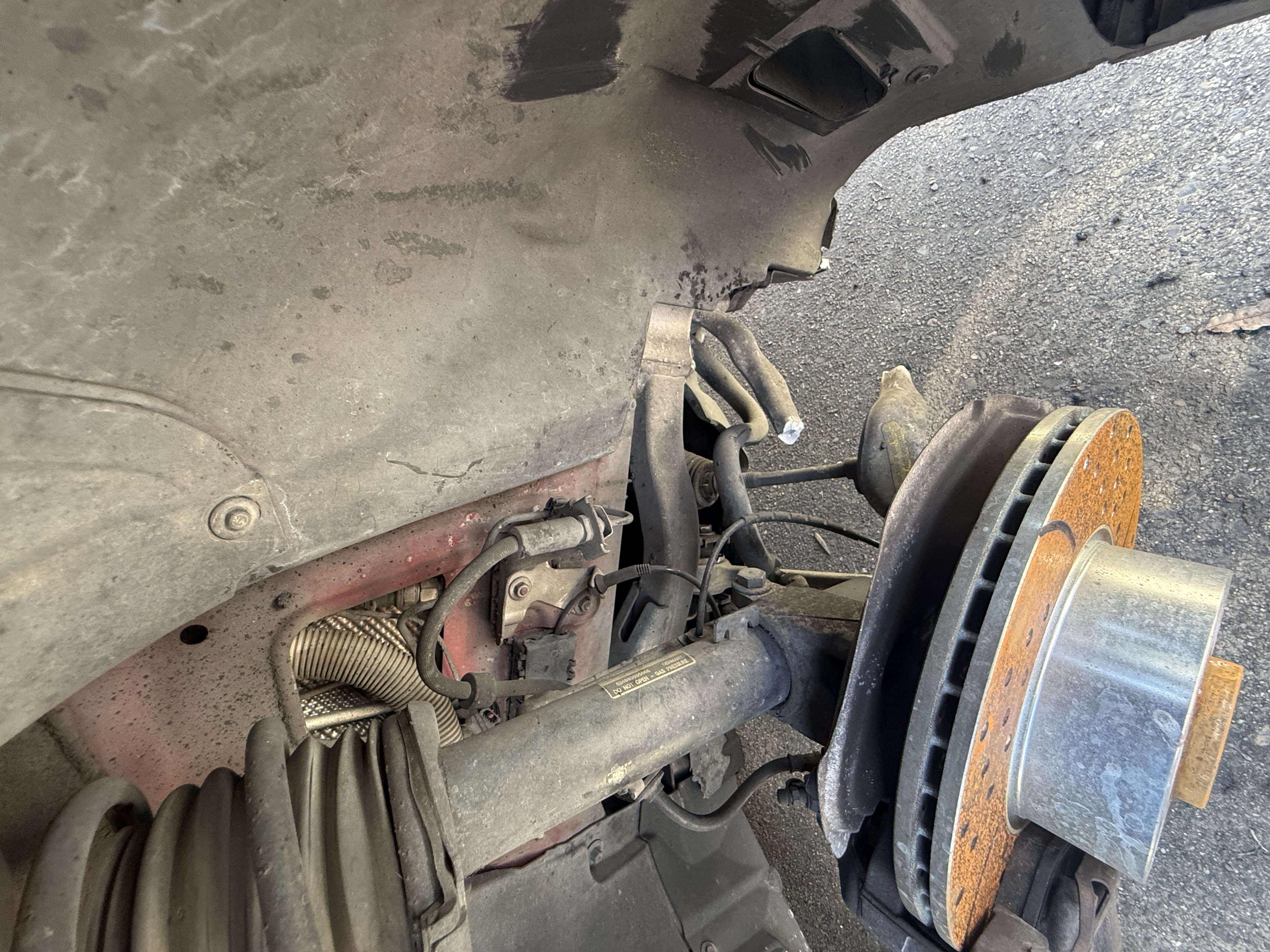 Front wheel removed to reveal rusted brake rotor, caliper, and exposed suspension components.