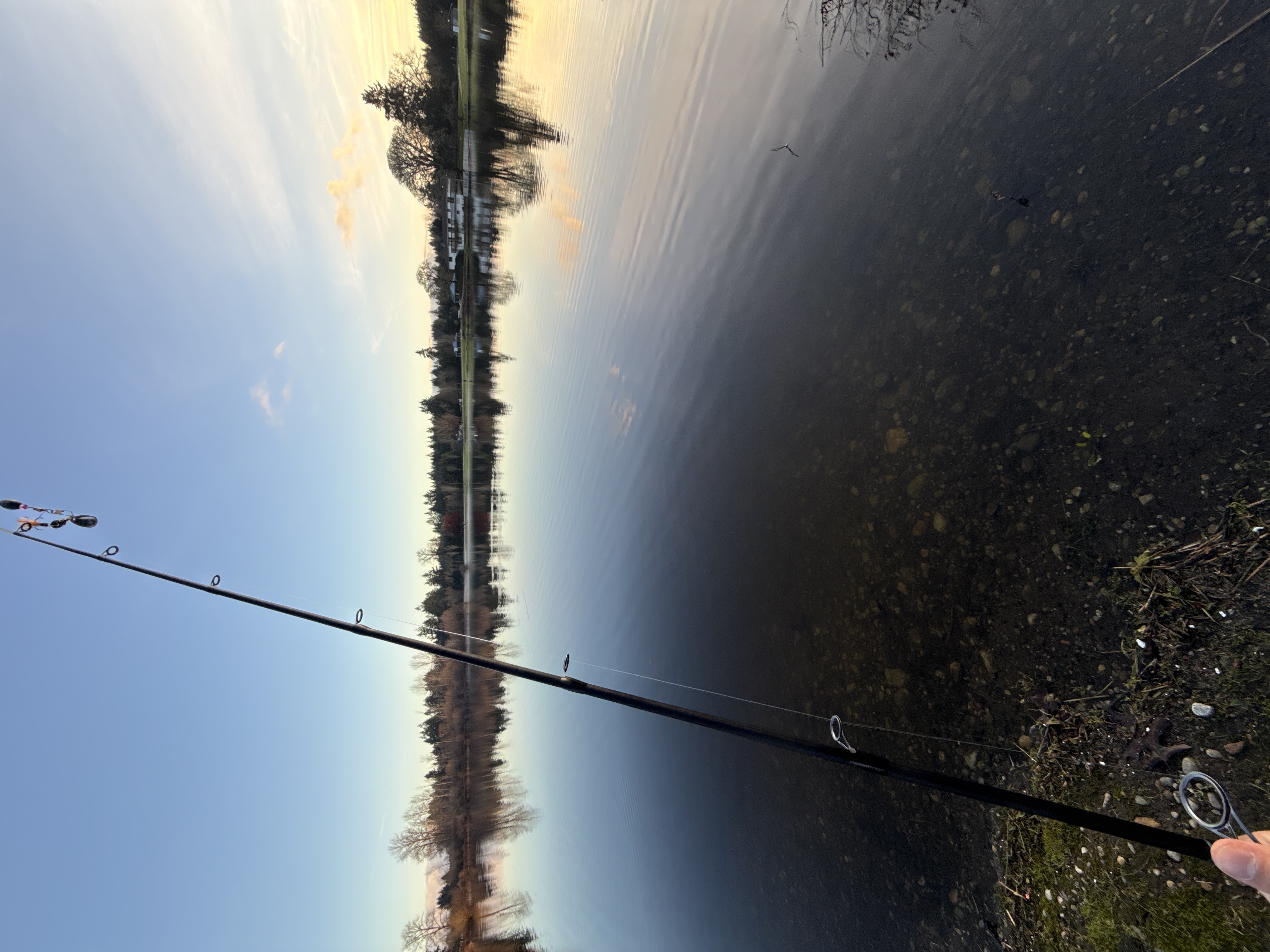 Calm lakeside fishing scene with a rod resting along the rocky shoreline at sunset