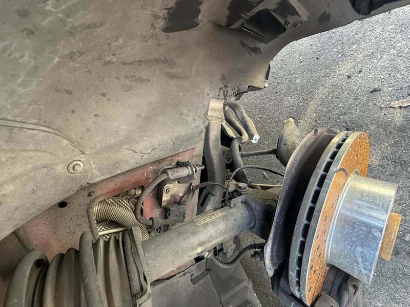 Close-up of a dusty vehicle front wheel with a rusty brake rotor and exposed suspension components.