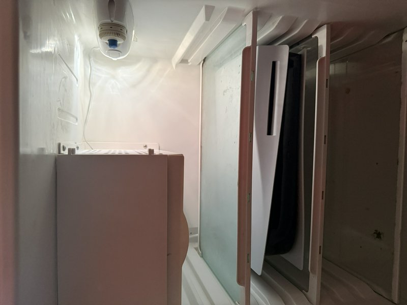 Compact utility bathroom with frosted glass shower door, white cabinet, and a ceiling security ca...