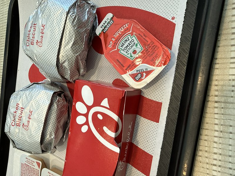 Chick-fil-A meal with wrapped sandwiches, a red chicken box, and sauce packets on a takeout tray.