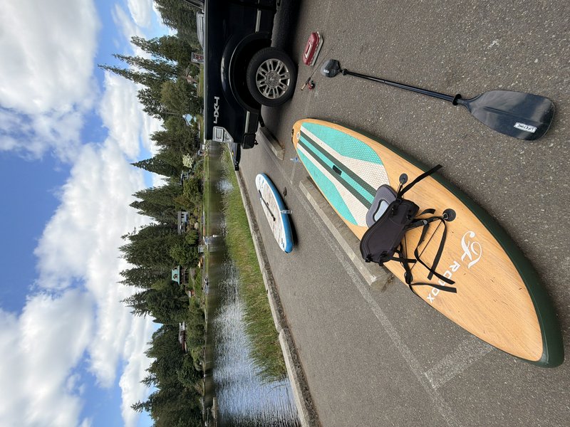 Paddleboarding gear including SUP boards and a paddle laid out next to a 4x4 truck parked at a tr...