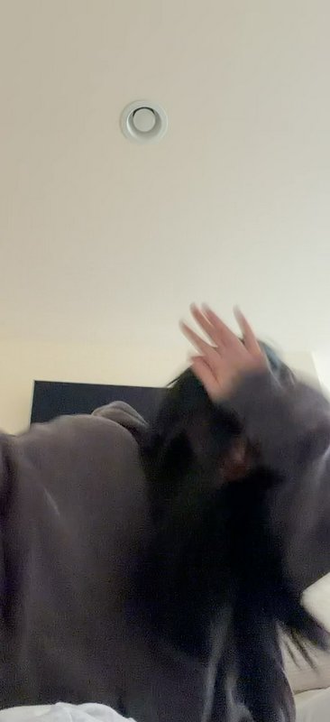 Motion-blurred low angle selfie of a person in a gray hoodie raising a hand to cover their face, ...