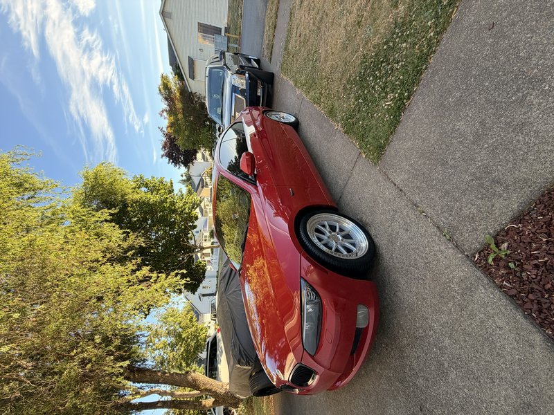 Glossy red modified sports car with aftermarket alloy wheels parked on a sunny suburban residenti...