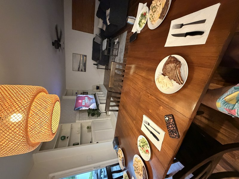 Wooden dining table set with plated steak meals and side salads in a cozy open-concept home