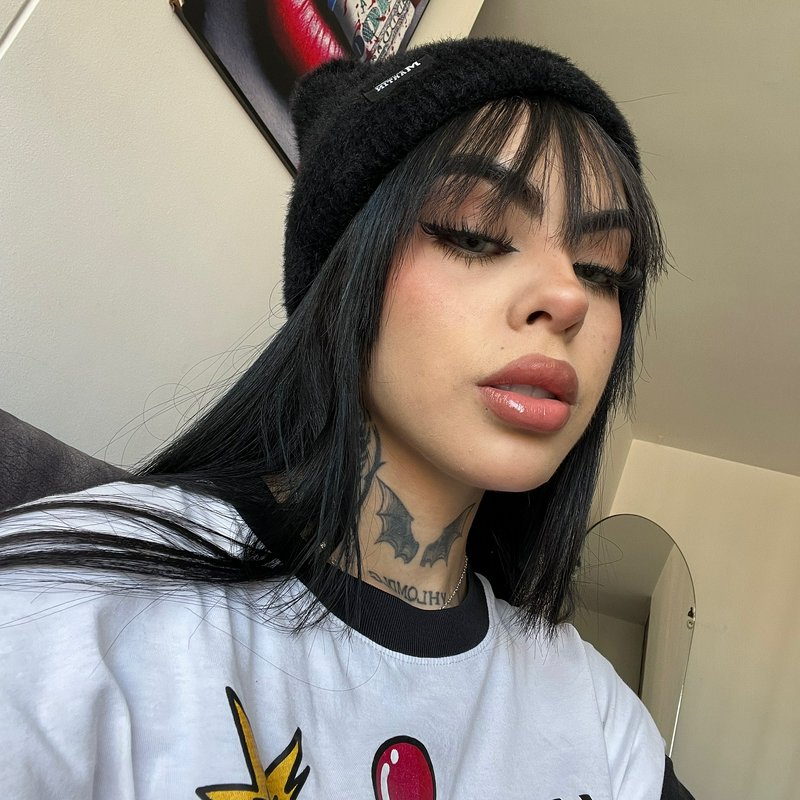 Selfie of alternative woman with bat neck tattoos, fuzzy black cat ear beanie, straight black hai...