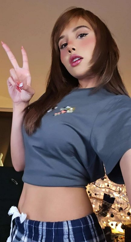 Young woman posing with a peace sign, wearing a cropped tee and plaid pajamas, with an anime filt...