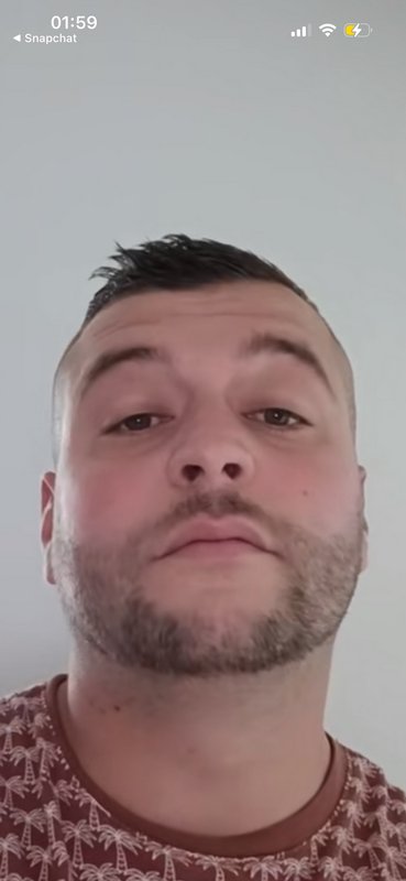Close-up Snapchat selfie of a bearded man with short spiky hair wearing a palm tree print t-shirt.