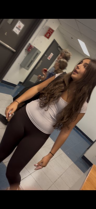 Surprised teen girl with long wavy brown hair stands in a school hallway looking upward