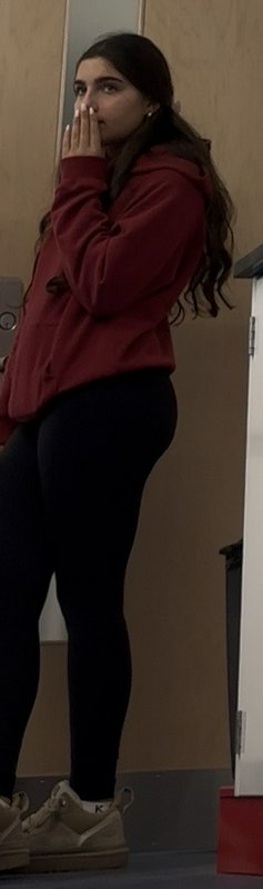 Young woman in a maroon hoodie holds her hand over her mouth while standing indoors
