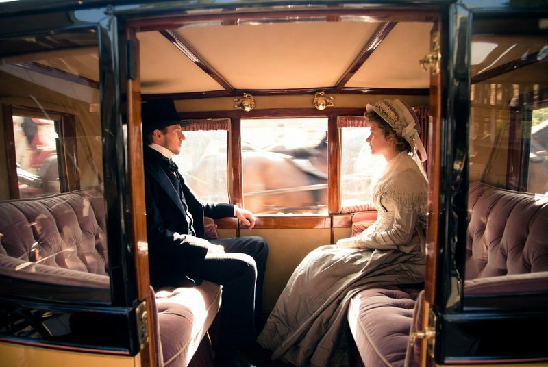 Vintage horse-drawn carriage interior with a man in dark suit and woman in a Victorian-era dress ...